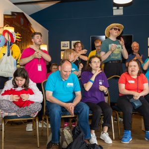 About 10 Include Choir members are performing at an event - some sat down and some standing up