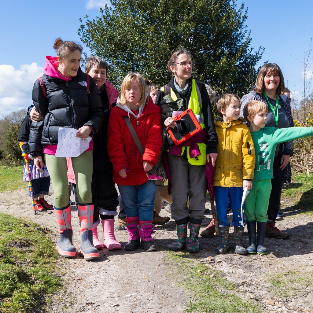 7 people a mix of ages on a walk in the countryside - stopped to look at something - one child is pointing
