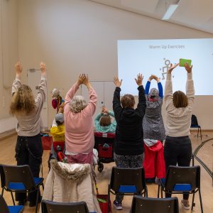The Include Choir in Epsom standing up and warming up - hands above heads!