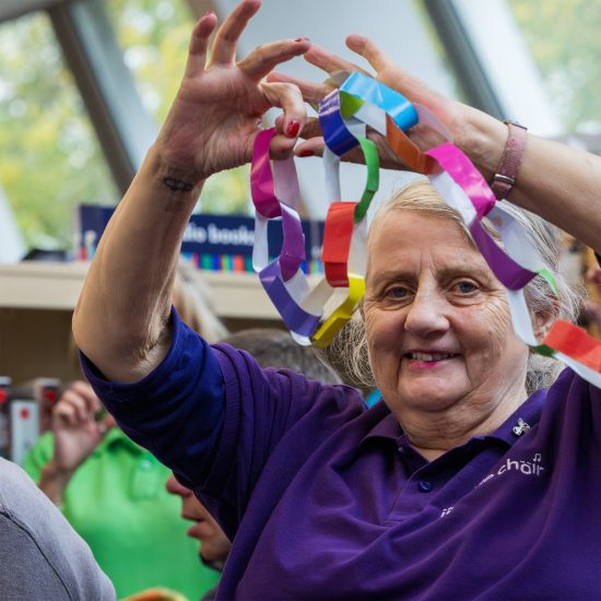 Include Choir member holding a paper chain smiling during a performance for World Singing Day