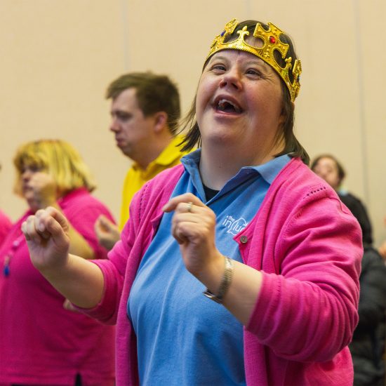 Ellie singing and smiling and moving at The Include Choir while wearing a gold dress-up crown